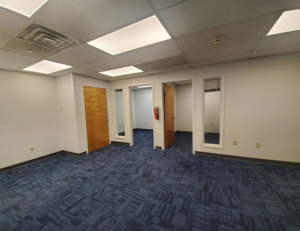 A vacant office space with blue carpet and doors available for lease.