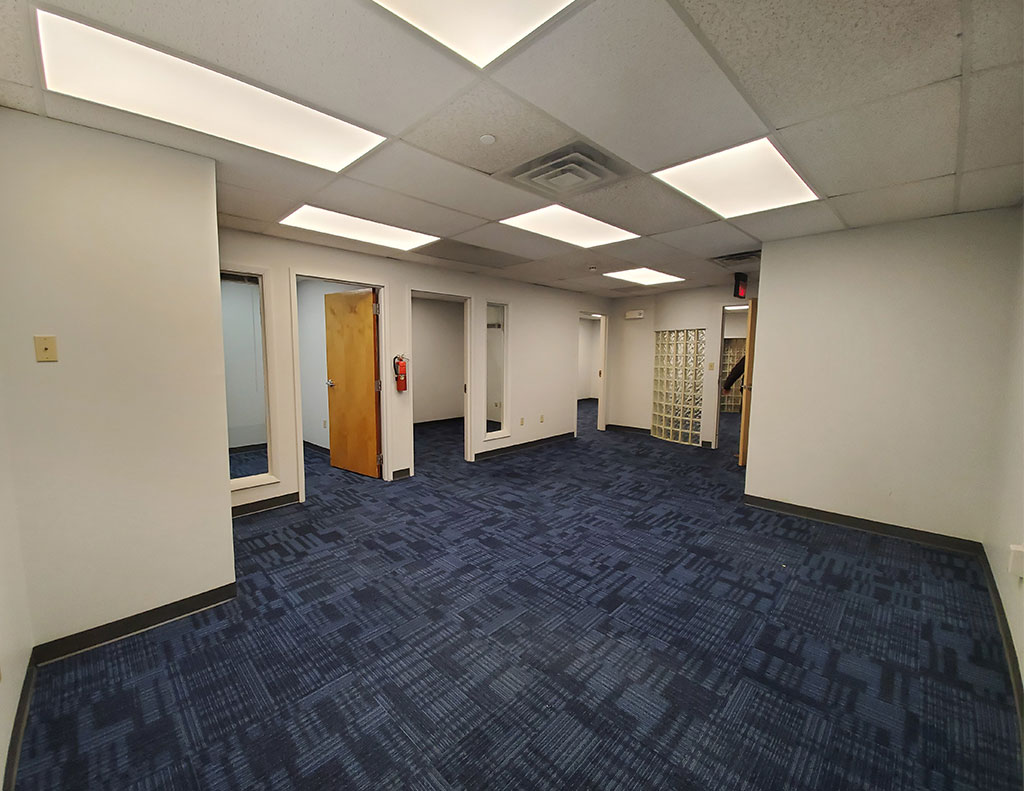 A pristine office space available for lease, featuring a minimalist design with calming blue carpet and clean white walls.