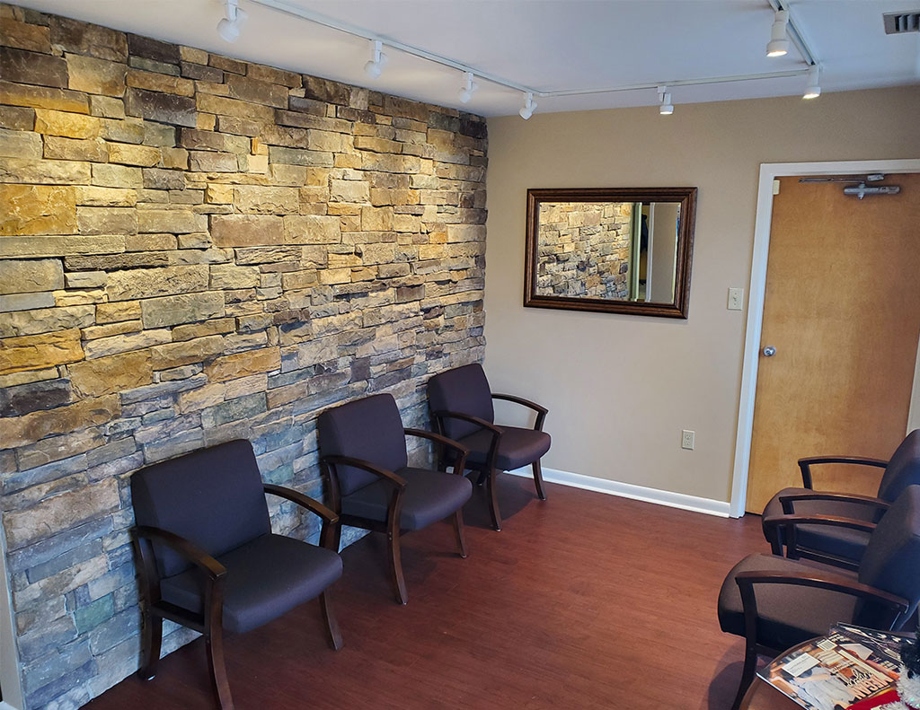 A spacious waiting room with comfortable chairs and a stylish stone wall, perfect for a 300 sq ft office space available for lease.