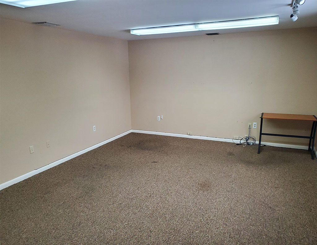A spacious office for lease, measuring 300 square feet and featuring plush carpeting and a sturdy desk.